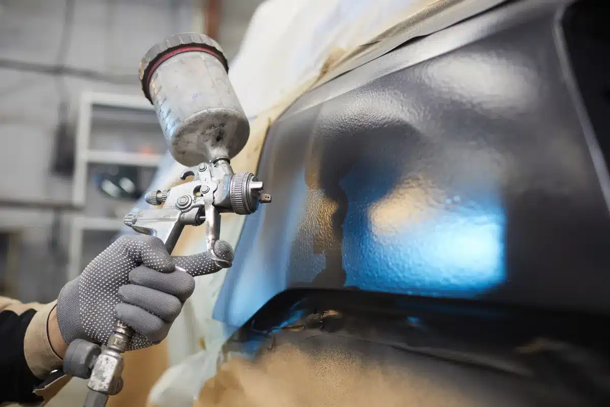Kuvassa automaalari maalaa autoa korkeapaine ruiskulla